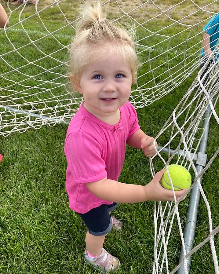 Toddler girl with a tennis ball in a net at The Club House childcare center.